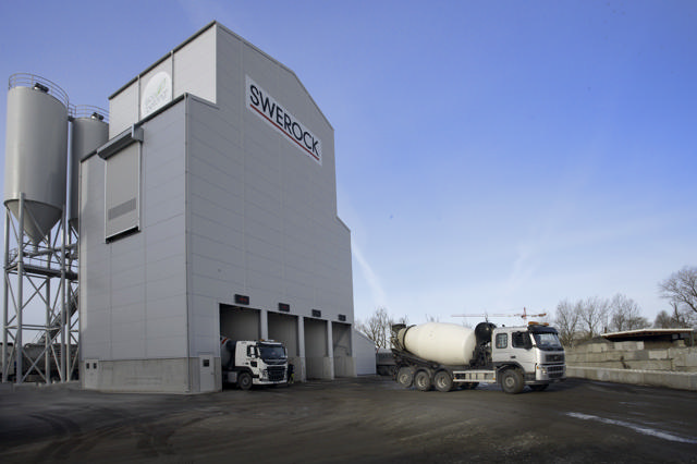 Mixing plant with 2 trucks parked in front if it.