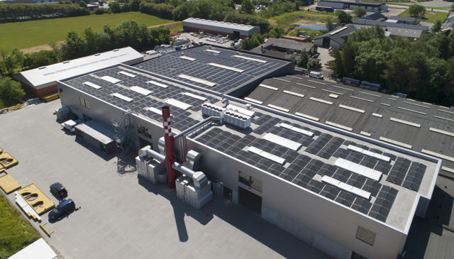 Aerial view of Haarup Maskinfabrik with solar panels on the roof and surrounding fields.