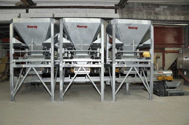 Three grey interchangeable hoppers pictured in a production hall.